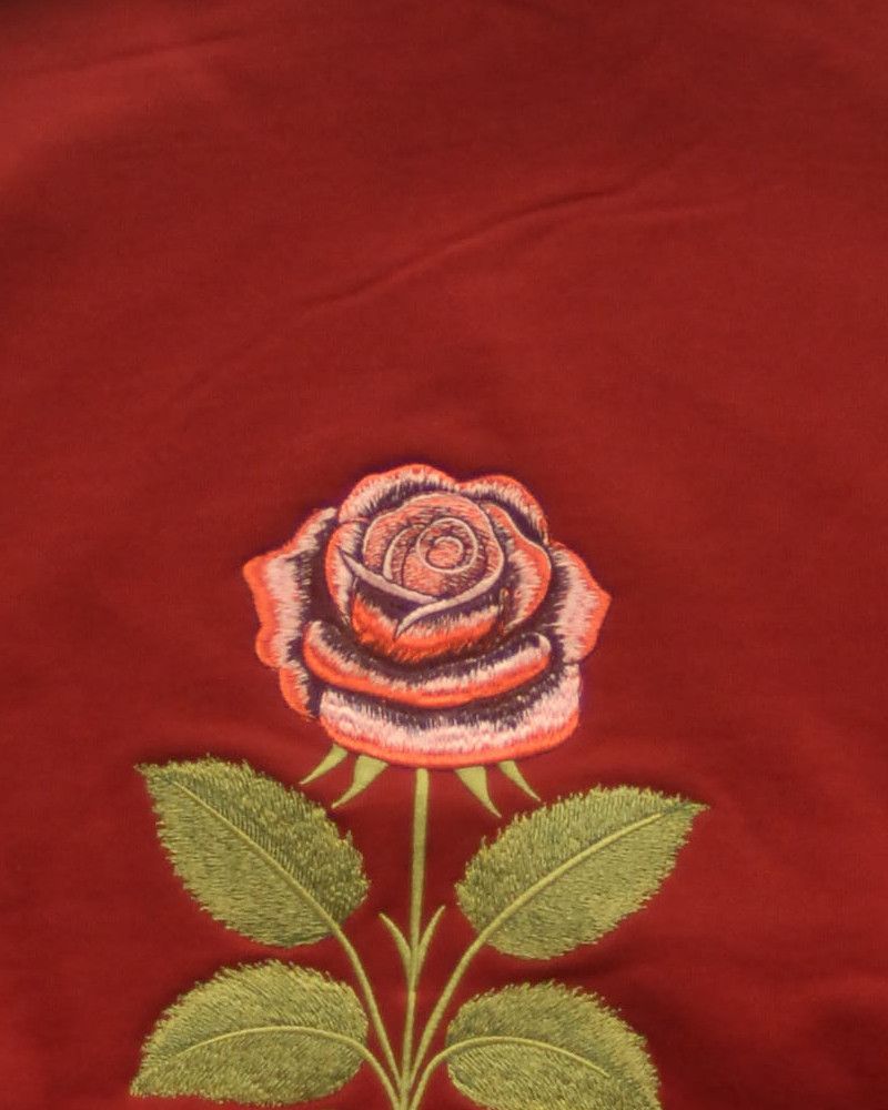 Dasselbe bordeauxfarbene Muster, etwas weiter entfernt aufgenommen, die Rose und zwei Blattpaare füllen das Bild.